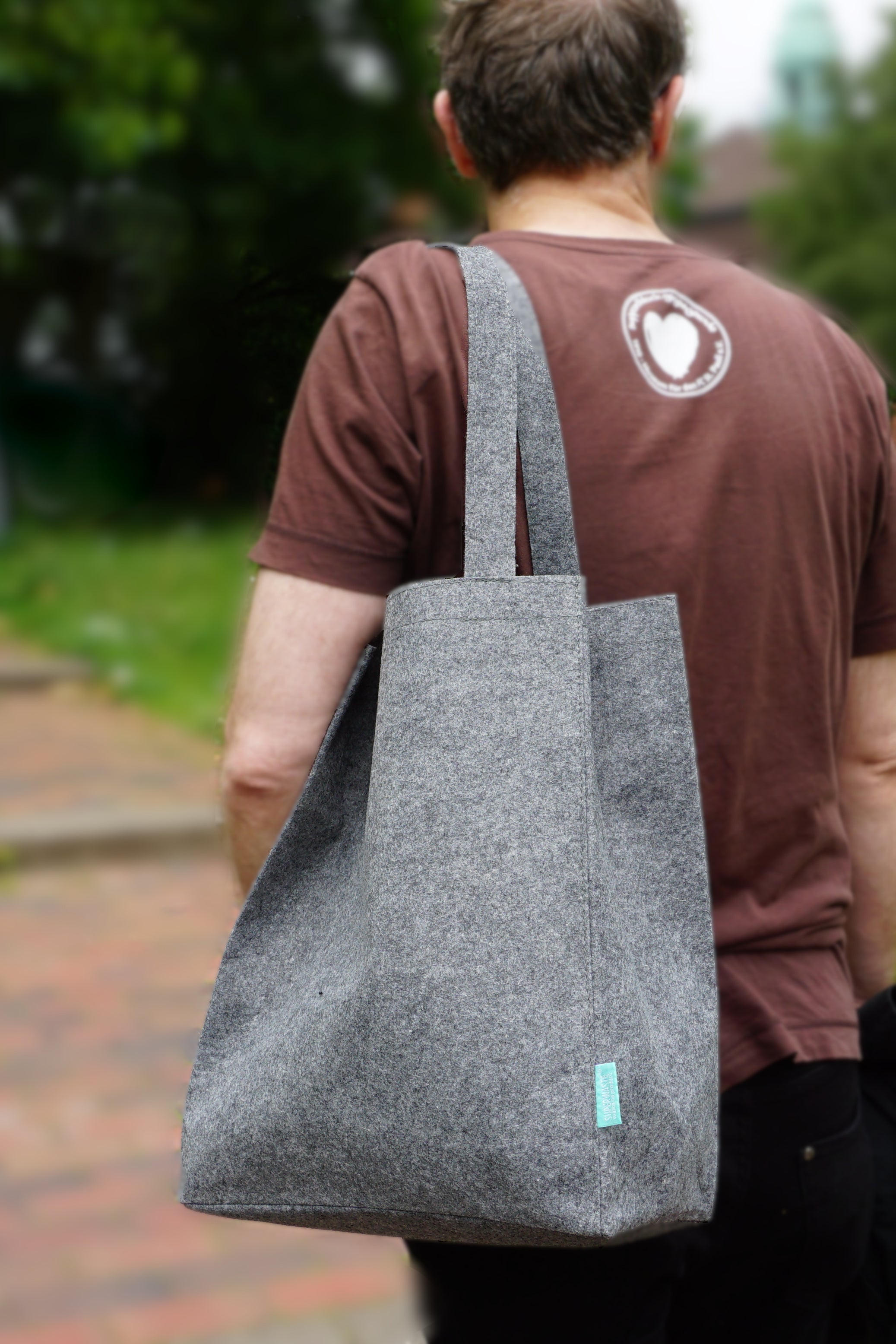 Mann mit einer grauen Tasche über die Schulter gehaengt.